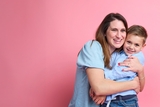 Mother and son in a warm embrace hug on pink background.