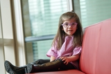 Girl with purple glasses with Neurological disorder sitting on couch.