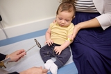 A baby being held by his mother is getting his reflexes checked at a Neurologist doctor appointment. 