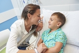 Parent smiling and holding the child’s hand while he’s laying down in a hospital bed.