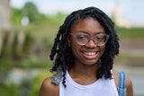 Smiling adolescent with curly black hair and purple reading glasses.