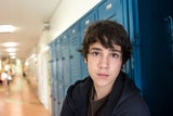 Boy standing against school blue lockers