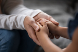 Comforting adult hands holding a teens hand