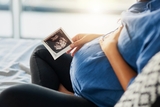 Pregnant woman looking at a sonogram with her hand resting on her abdomen