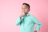 School age boy hold his hand to his chin, standing against a pink backdrop