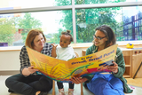 Two caregivers with a young child in a play kitchen.