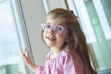 Young smiling girl wearing a pink checkered dress and purple glasses