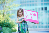 Little girl standing outside holding a sign that reads, "Thank You!"