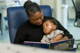 Newborn looking at mom while she reads him a book