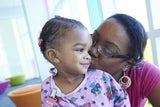 Mother kissing cheek of daughter in hospital gown