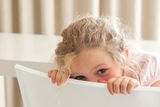 Shy girl hiding her face behind a chair