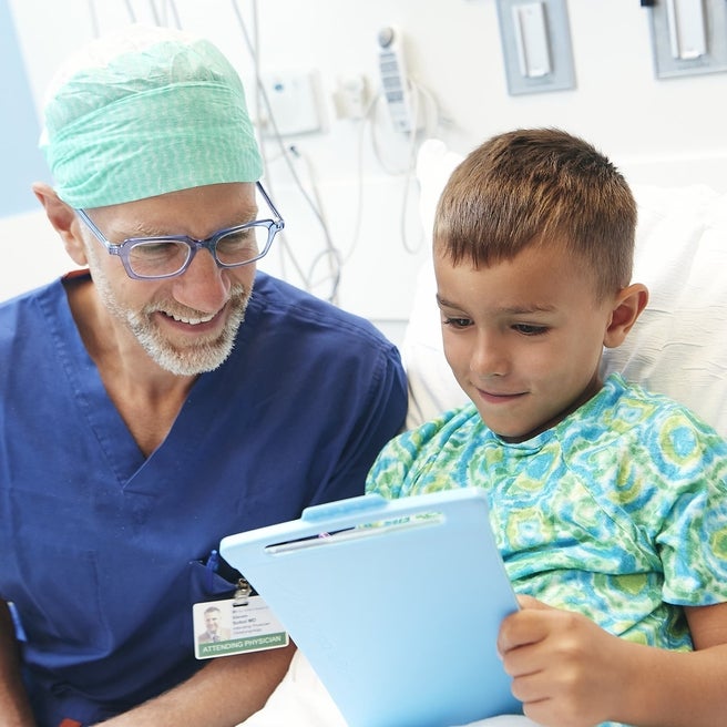 Blonde boy in hospital bed showing a game to his pediatrician