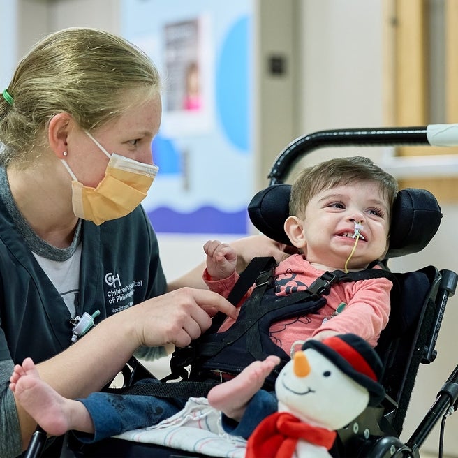 Nurse tickling smiling baby boy that has a feeding tube.