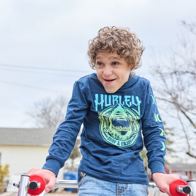 A curly-haired boy with a neurological condition using crutches to assist with walking.