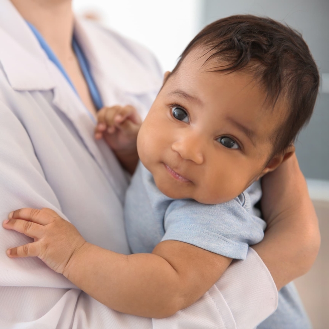 Infant looking up, in doctors arms.