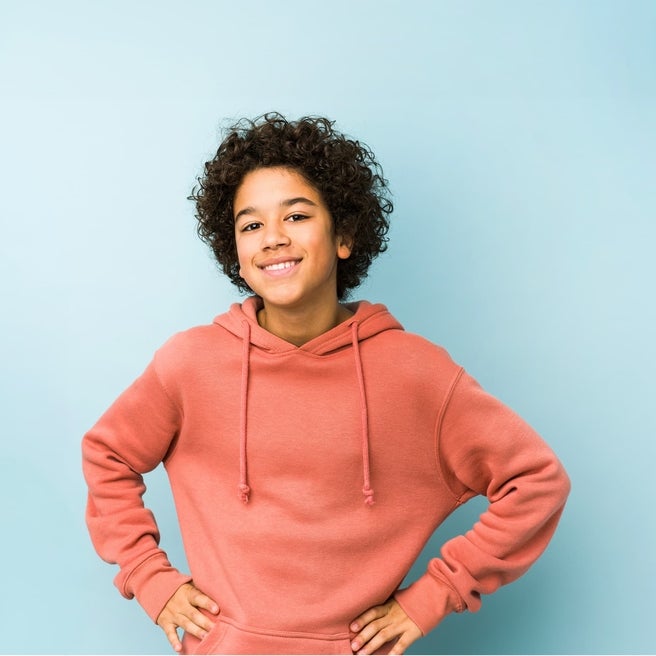 Teenager smiling with hands on their hips, wearing a coral sweatshirt.