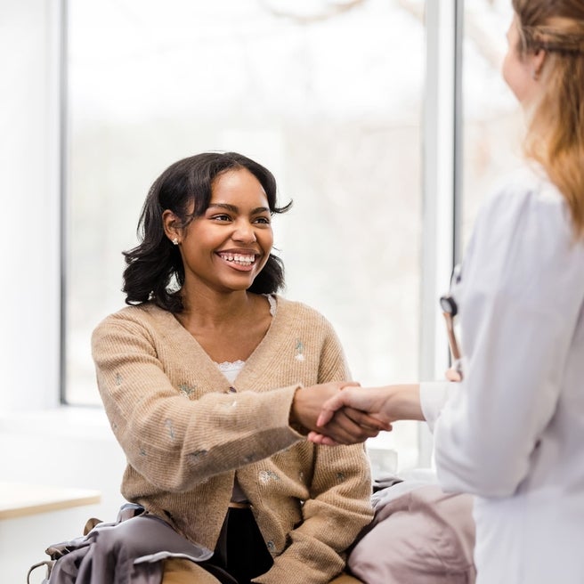 Older girl smiling and  shaking hands with female doctor in white coat.