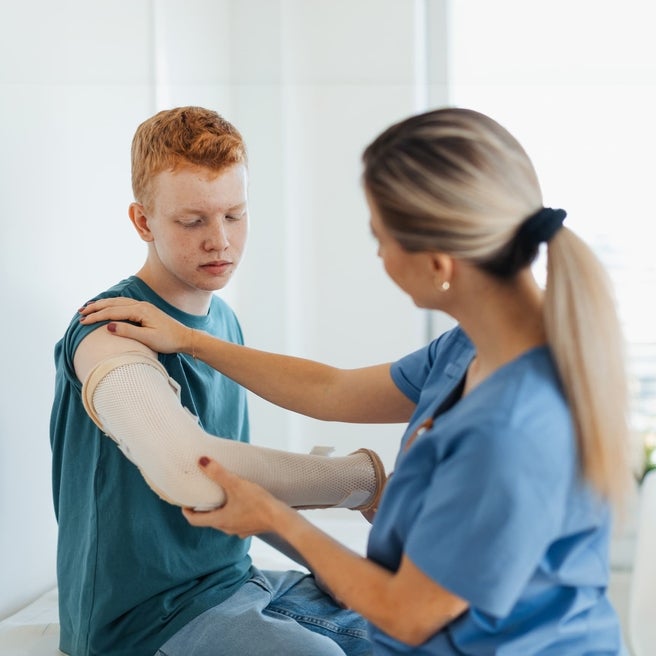 Doctor helping teen boy with broken arm.