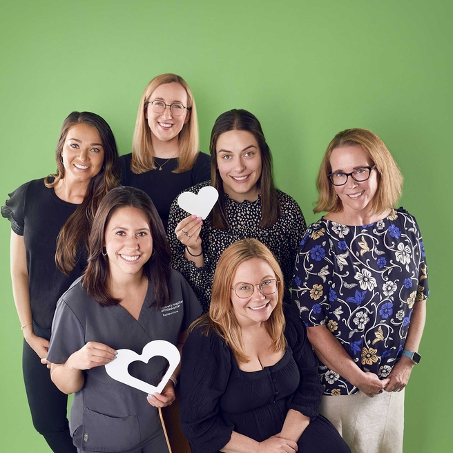 A group of oncology staff holding heart symbols and smiling.