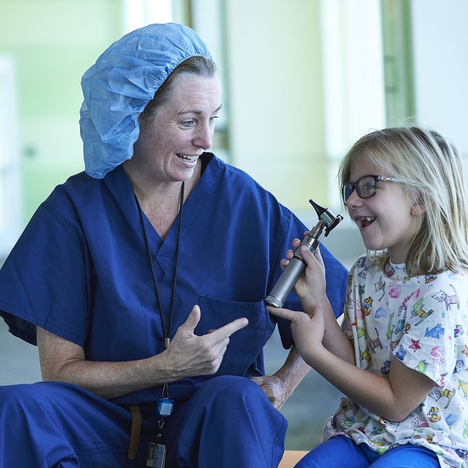 Female doctor and blonde girl smiling while holding an otoscope