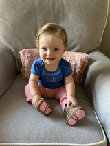 Baby girl with pink pants and blue t-shirt smiling on arm chair