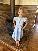 Young girl with blond hair, light blue dress, barefoot posing in front of a furnace