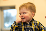 2-year-old toddler boy in flannel button-down shirt pointing to his nose.