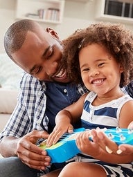 Father helping young daughter play ukulele