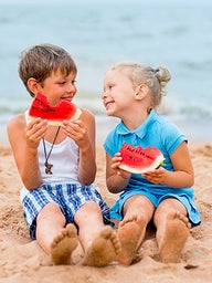 Two kids on the beach eating watermelon