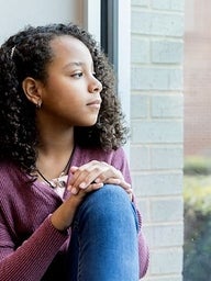 Adolescent girl sadly looking out window