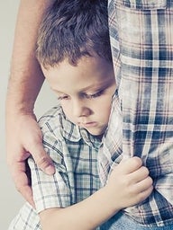 Young boy clinging to parent's leg