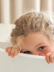 Shy girl hiding her face behind a chair