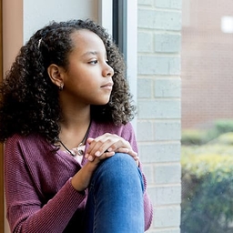 Adolescent girl sadly looking out window