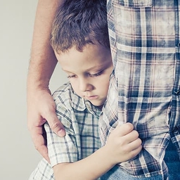 Young boy clinging to parent's leg