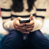 Teen sitting on a bed, holding a cell phone