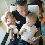 Caucasian male father reading a book to toddler and infant.